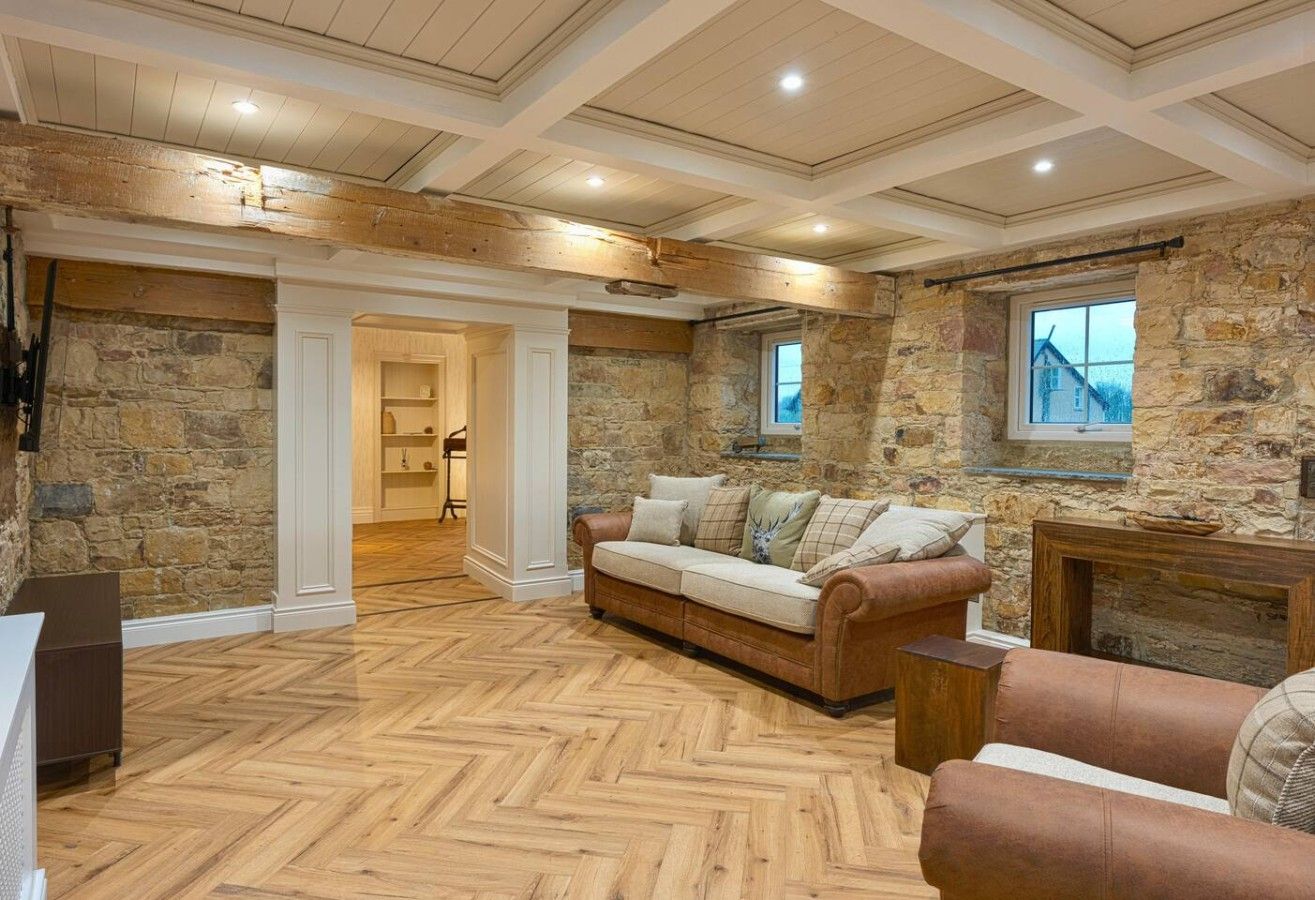 A room with a herringbone floor, stone walls, a fireplace, and a sofa.