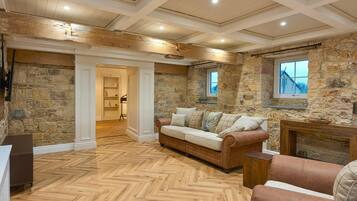 A room with a herringbone floor, stone walls, a fireplace, and a sofa.