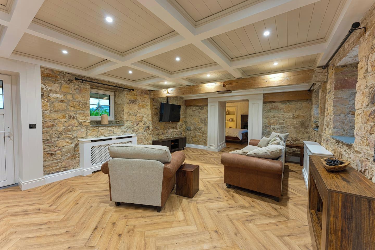 A spacious room with a stone wall, wooden flooring, a television, and a cozy seating area with sofas and a coffee table.