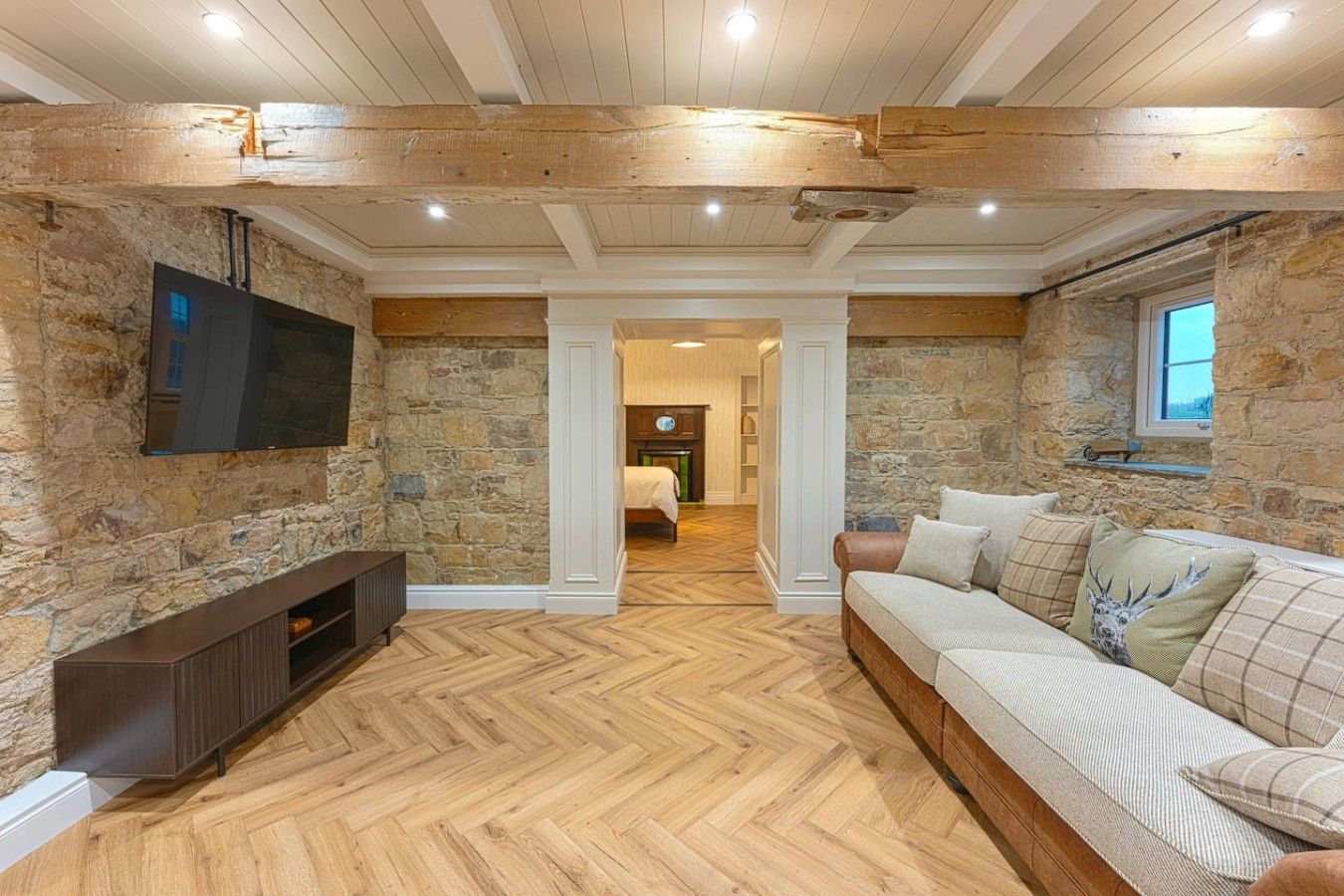 Una habitación con paredes de piedra, piso de madera, un televisor montado en la pared y un sofá con cojines.