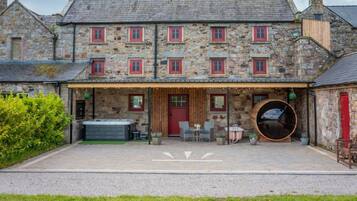 A stone building with a covered patio, outdoor seating, and a hot tub.