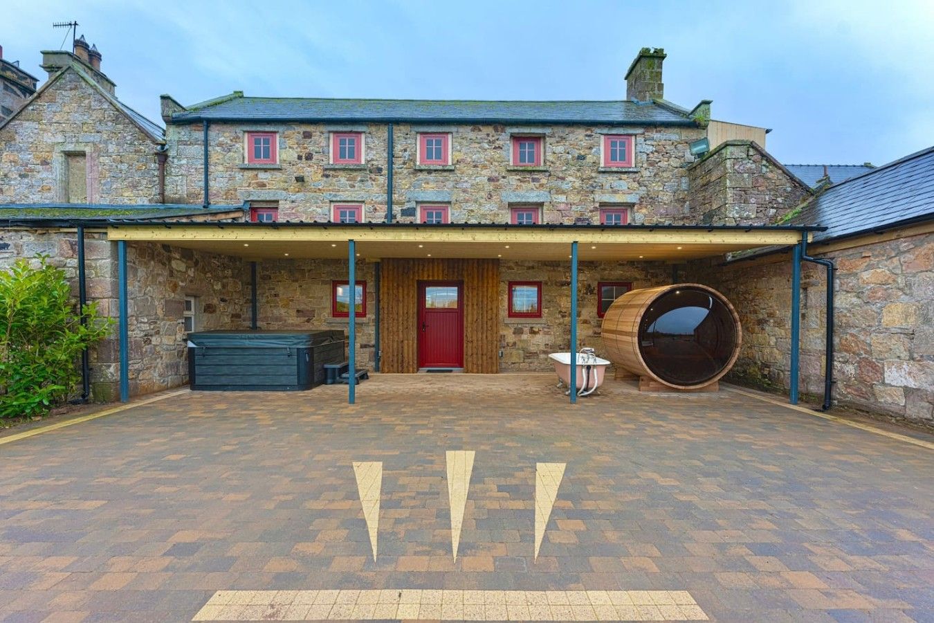 A stone building with a covered entrance, a red door, and a large barrel.
