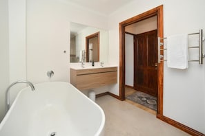 Un baño con una bañera independiente, un tocador de madera, un espejo y un perchero para toallas.