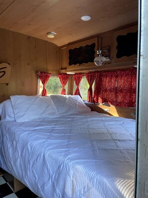 A room with a bed, wooden walls, a window with red curtains, and a ceiling light.