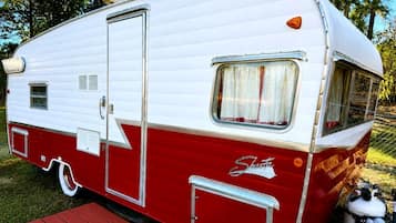 A vintage Shasta trailer with a side door, a small window, and a storage compartment.