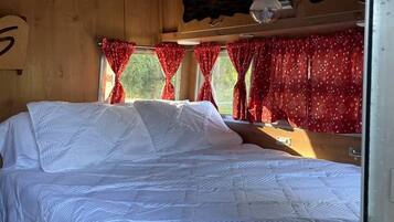 Una stanza con un letto, pareti in legno, una finestra con tende rosse e una luce a soffitto.