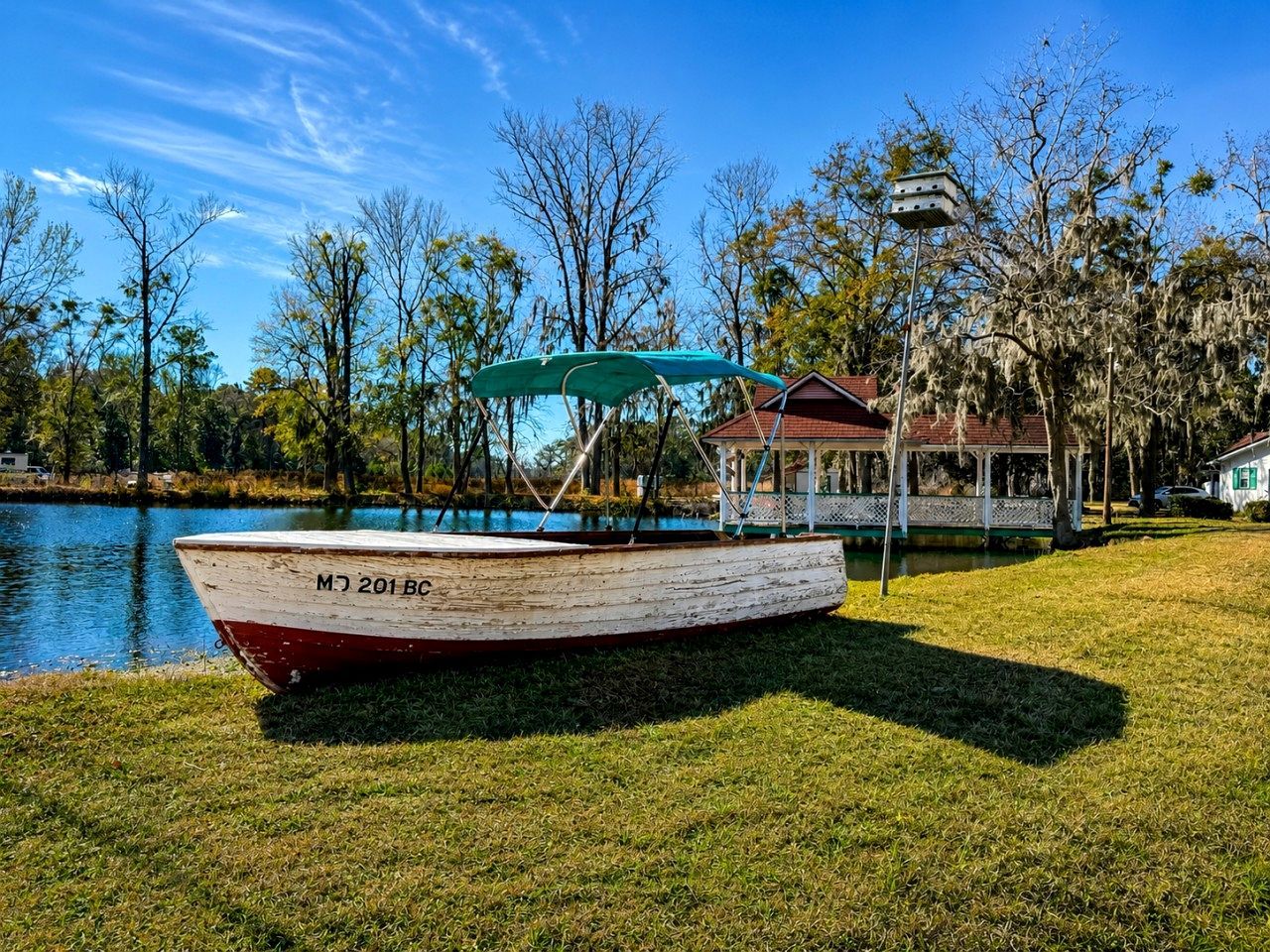 A boat with the number 'MJ 201 BC' on a grassy area near a body of water, with a gazebo and a house in the background.