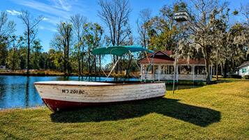 A boat with the number 'MJ 201 BC' on a grassy area near a body of water, with a gazebo and a house in the background.