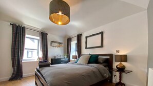 A bedroom with a large bed, a bedside table with a lamp, a window with curtains, and a wall-mounted picture frame. - Secluded converted stables in the heart of the Mourne Mountains. Pet friendly! (Bryansford)