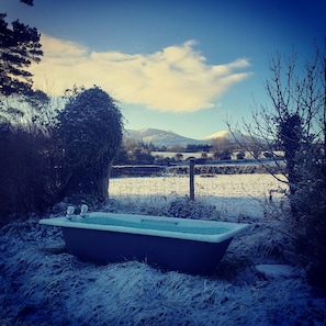 Eine Badewanne in verschneiter Outdoor-Umgebung mit Blick auf ein Feld und Berge im Hintergrund.
