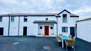 A two-story building with a red door, a garage, and a dining area with chairs and a table. - Secluded converted stables in the heart of the Mourne Mountains. Pet friendly! (Bryansford)