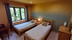 Ein Zimmer mit zwei Einzelbetten, einem Schreibtisch, einem Stuhl und einem fenster mit Vorhängen.