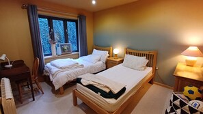 Ein Zimmer mit zwei Betten, einem Schreibtisch, einem Stuhl, einem Fenster mit Vorhängen und einer Lampe.