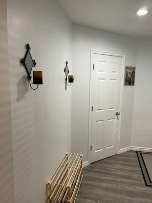 A hallway with a white door, a wall-mounted light fixture, and a wooden rack. - Charming Vacation Rental with Pool & Pet-Friendly Stay in Kanab, Utah (Kanab)