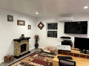 A living room with a fireplace, a flat-screen TV, a computer, and a gaming chair. - Charming Vacation Rental with Pool & Pet-Friendly Stay in Kanab, Utah (Kanab)