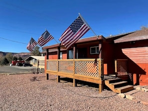 A red building with a wooden deck and two American flags. - Charming Vacation Rental with Pool & Pet-Friendly Stay in Kanab, Utah (Kanab)
