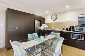 A modern kitchen with dark cabinets, a glass dining table, and white chairs. - Seabatical Retreat minutes from the beach (Auckland)