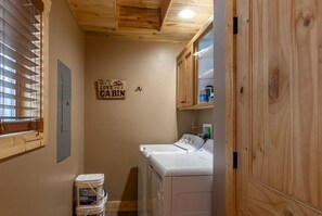 Ein Waschraum mit Waschmaschine, Trockner, Holzausbau, einem Fenster mit Jalousien und einem Schild an der Wand.