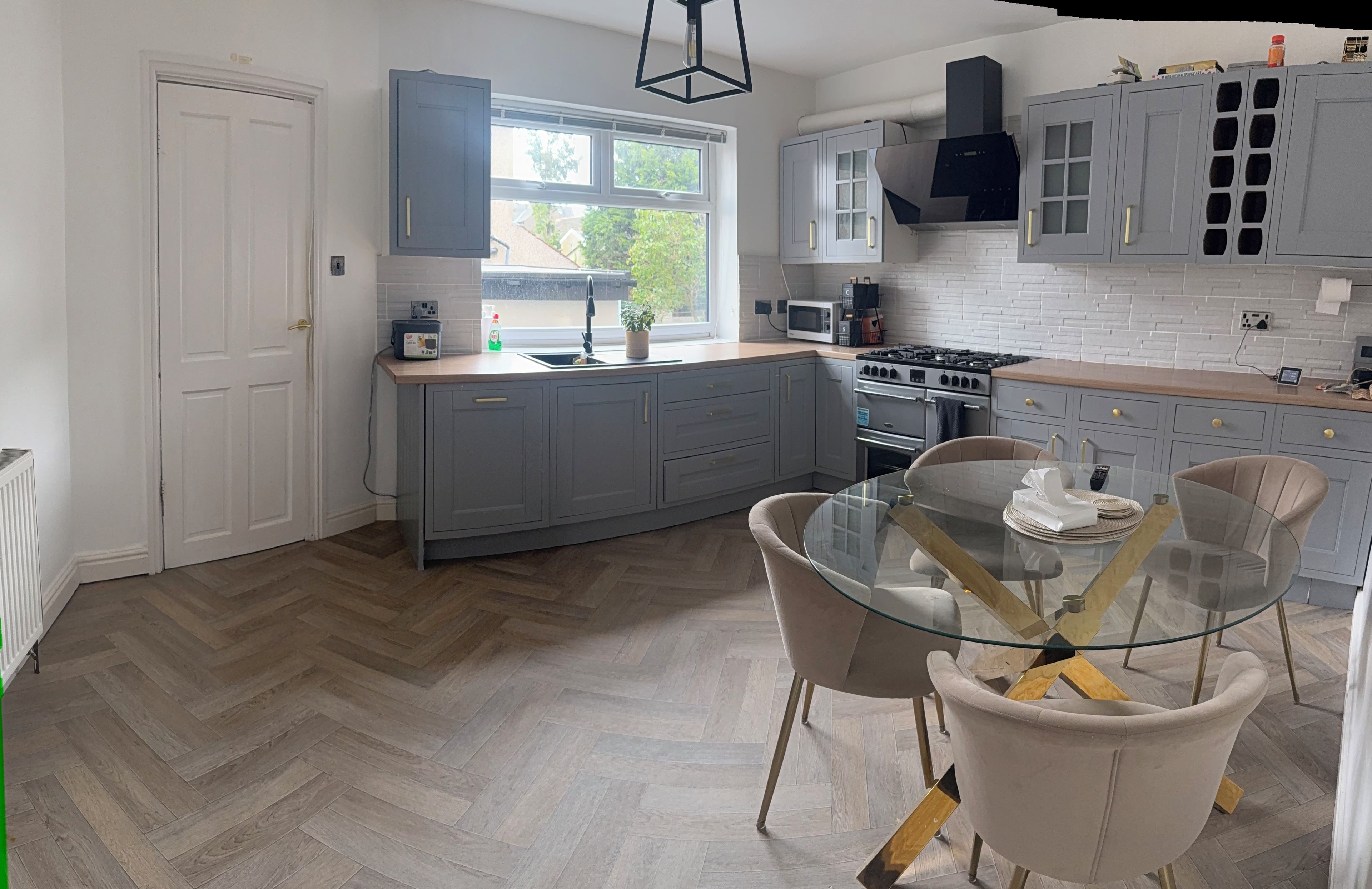 Una cocina moderna con armarios grises, una mesa de comedor de vidrio y un suelo de madera en patrón de espiga.