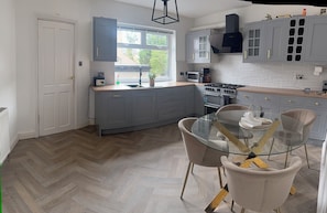 Una cocina moderna con armarios grises, una mesa de comedor de vidrio y un suelo de madera en patrón de espiga.