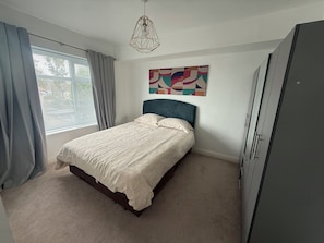 A bedroom with a bed, curtains, a wall art piece, and a wardrobe.