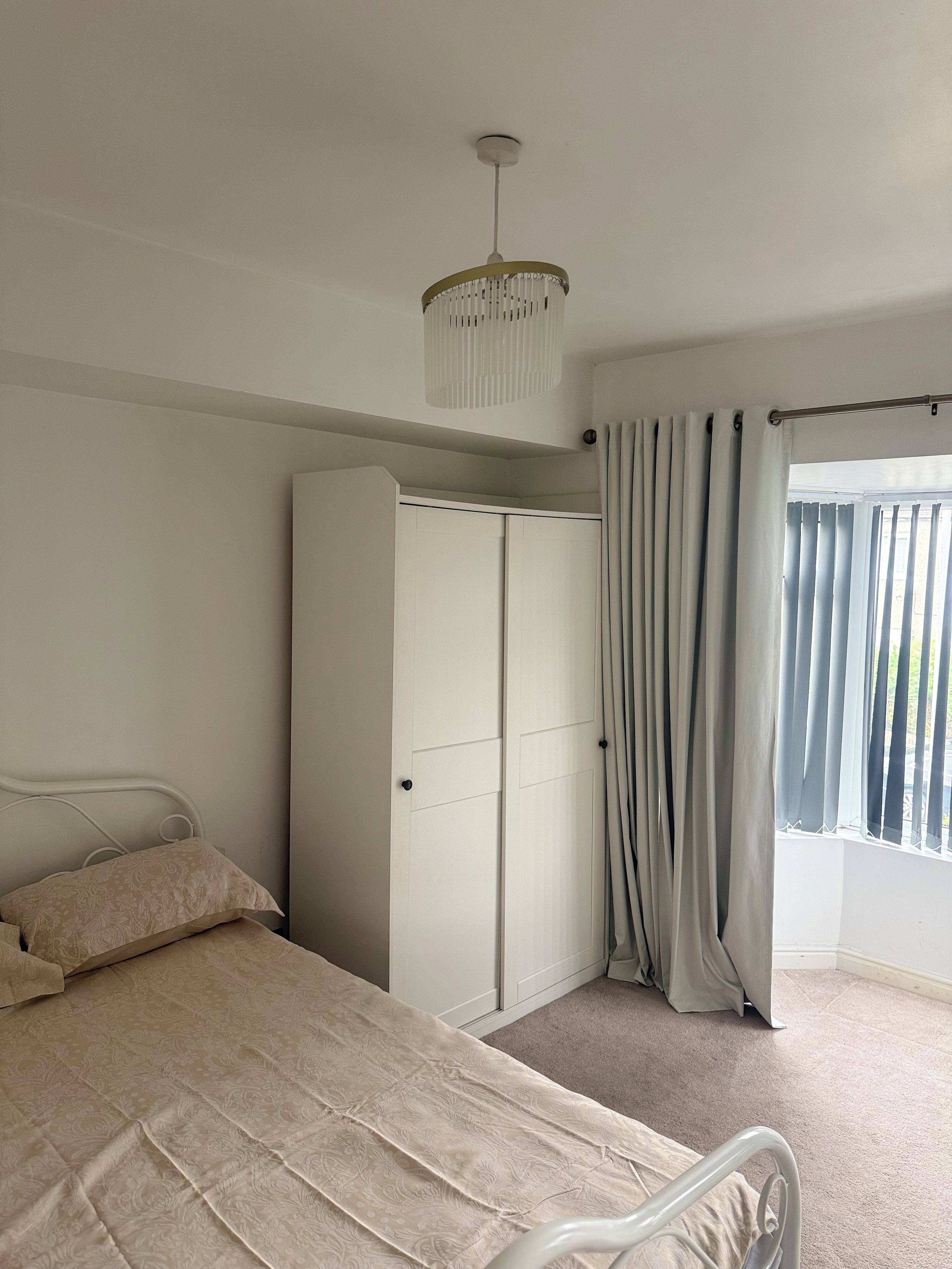 A bedroom with a bed, a wardrobe, a curtain, and a ceiling light fixture.