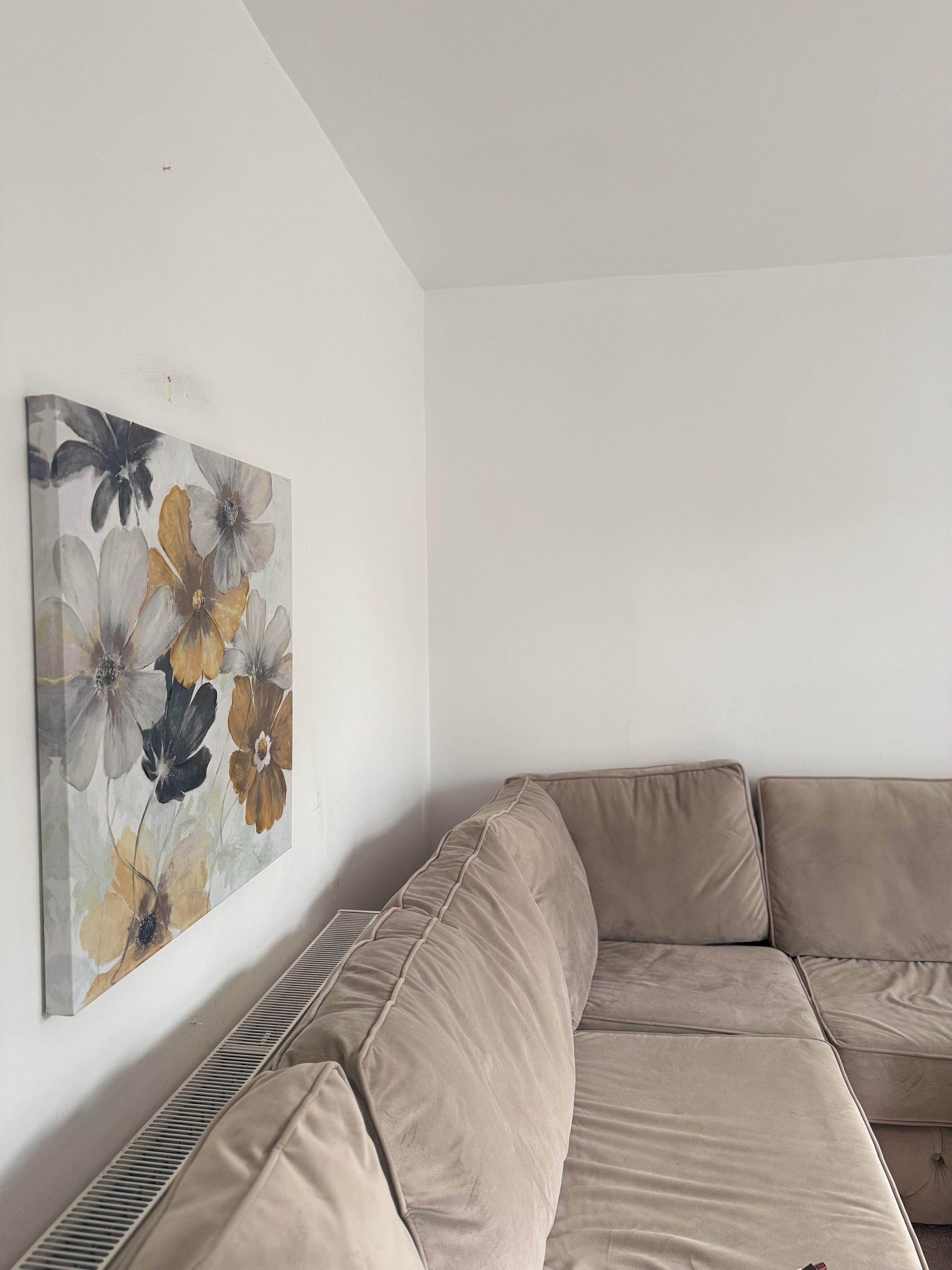 Un sofá seccional beige frente a una pared blanca con una obra de arte floral.