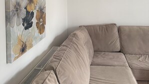 En beige hjørnesofa foran en hvid væg med et blomsterbillede.