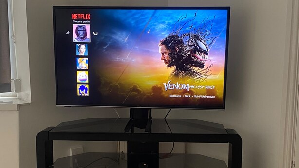 Et fjernsyn på et sort stativ, der viser Netflix-grænsefladen med filmen 'Venom: The Last Dance'.