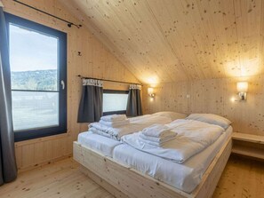 A wooden cabin bedroom with a bed, two windows, and a view of the outdoors. - One-bedroom Cabin (Sankt Georgen am Kreischberg)