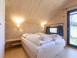 Une chambre dans une cabane en bois, avec un lit, deux lampes fixées au mur, une fenêtre avec des rideaux et une porte.