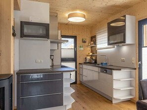 A compact kitchen with a microwave, stove, and modern cabinetry. - One-bedroom Cabin (Sankt Georgen am Kreischberg)