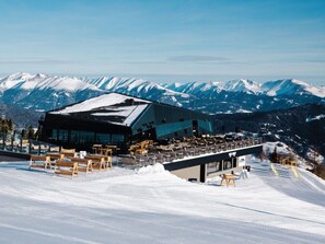 Un bâtiment moderne à la façade de verre, entouré de montagnes enneigées.