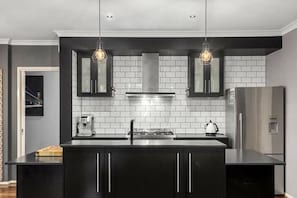 Una cocina moderna con armarios negros, una campana de acero inoxidable e iluminación colgante.