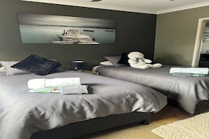 Un dormitorio con dos camas, una mesita de noche, una lámpara, un osito de peluche y un cuadro en la pared.