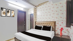 Quarto com cama, mesa de cabeceira, um vaso de flores e uma porta.