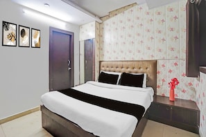 Un dormitorio con cama, mesita de noche, un florero con flores y una puerta.