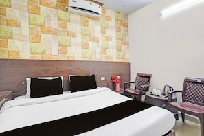 Una habitación de hotel con cama, una silla, una mesita y un equipo de aire acondicionado en la pared.