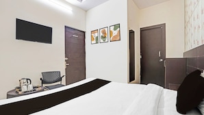 Quarto de hotel com cama, uma cadeira, uma mesa pequena com chaleira e chávenas, e três quadros nas paredes.