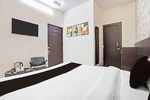 Habitación de hotel con cama, una silla, una mesita con tetera y tazas, y tres cuadros en la pared.