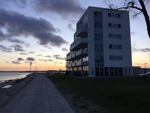 Ein mehrstöckiges Gebäude mit Balkonen, einem gepflasterten Weg und einem Gewässer im Hintergrund.