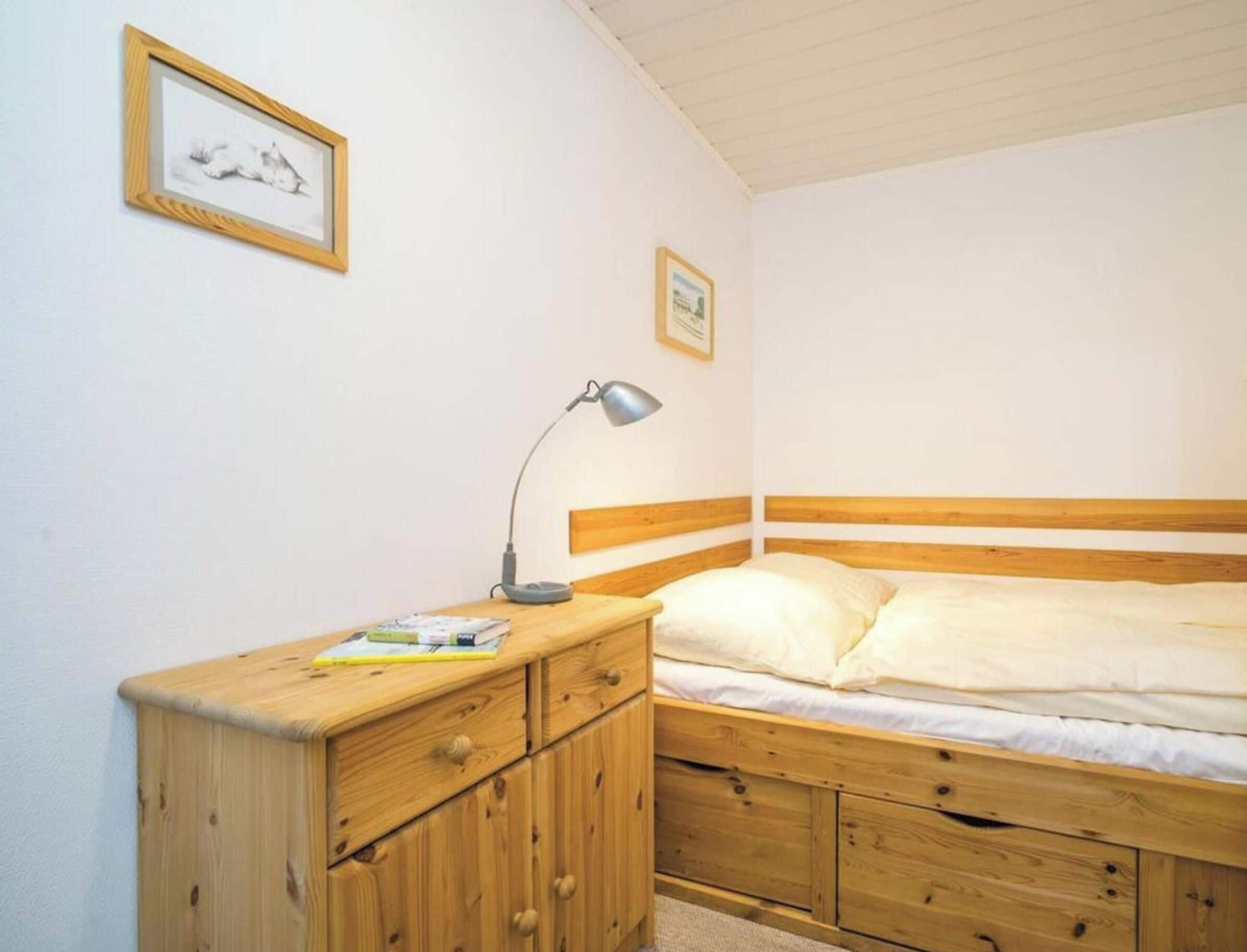 Ein Schlafzimmer mit einem hölzernen Bett, einem Nachttisch mit Lampe und zwei gerahmten Bildern an der Wand.