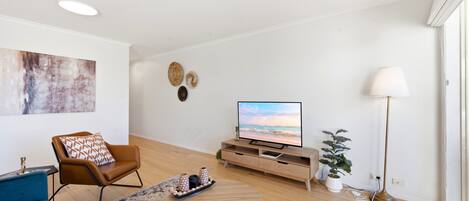 A modern living room with a flat-screen TV, a brown leather sofa, a coffee table, and a potted plant.
