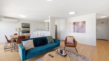 A modern living room with a blue sofa, a coffee table, and a dining area with chairs.