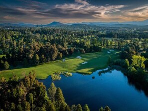 A golf course with a lake, surrounded by dense forest and distant mountains. - Spacious 2-bedroom Retreat With Golf Course Views (Canberra)