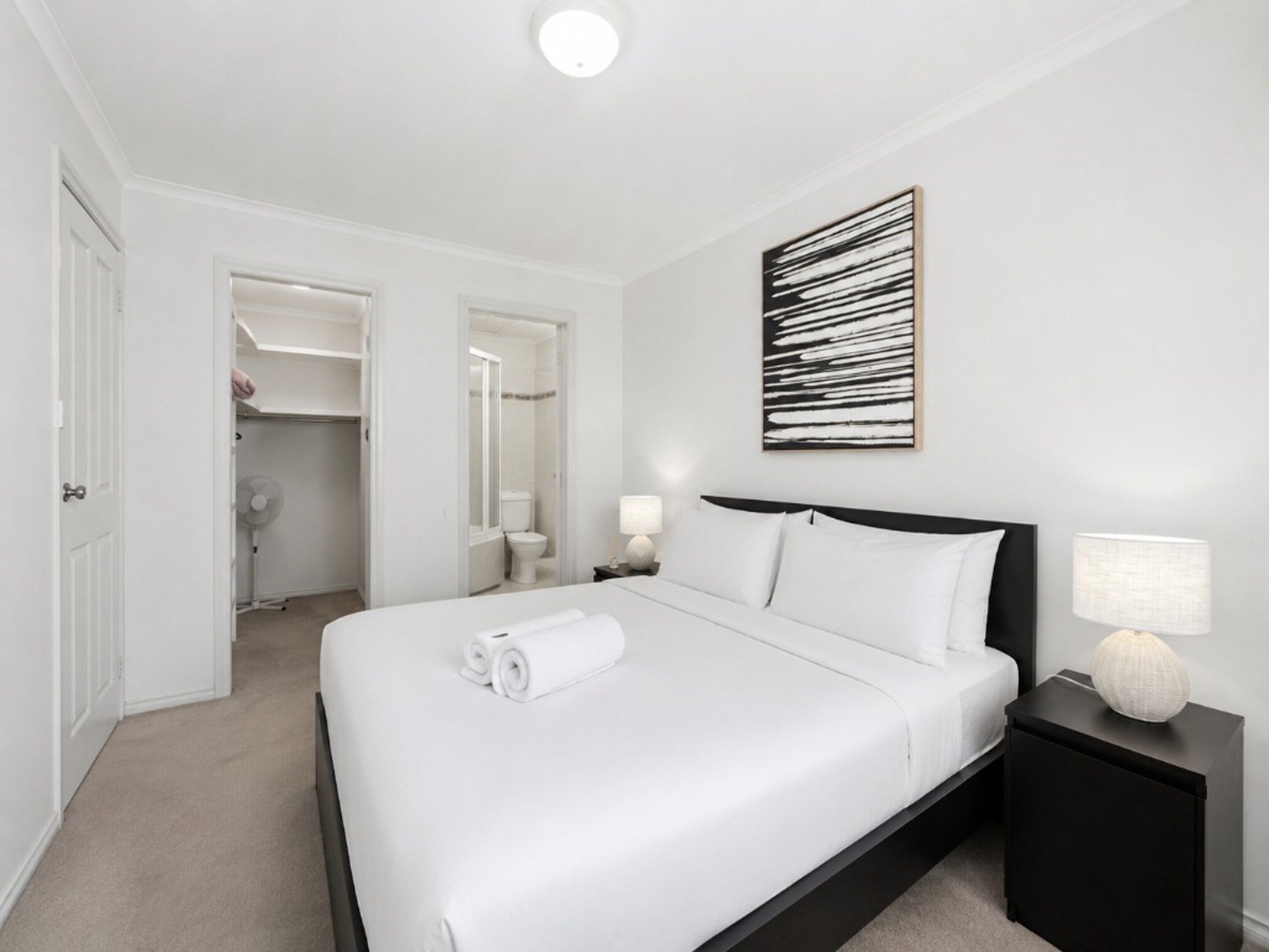 A hotel room with a bed, bedside tables, a wall-mounted artwork, and a bathroom visible through an open door.