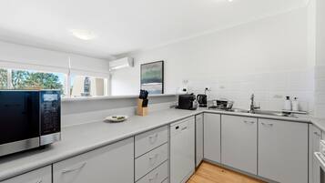 A modern kitchen with grey cabinets, a built-in dishwasher, a coffee maker, and a window with a view of trees.
