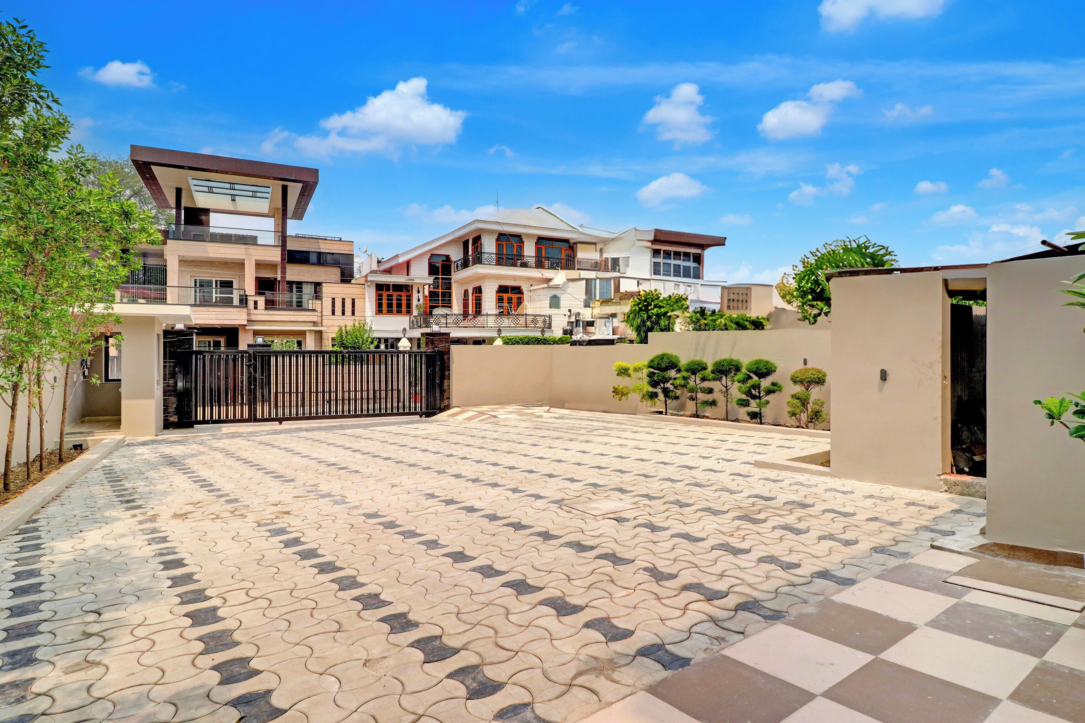 Zona residencial com pátio pavimentado, entrada com portão e casa de vários andares com varandas.
