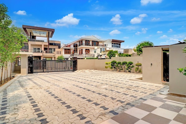 Zona residencial con un patio empedrado, entrada protegida por una reja y una casa de varios pisos con balcones.