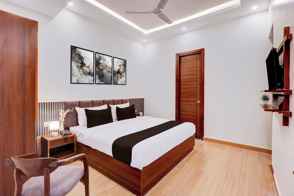 Une chambre moderne avec un lit en bois, une table de chevet avec une lampe, une chaise, un ventilateur de plafond et des œuvres d’art accrochées au mur.